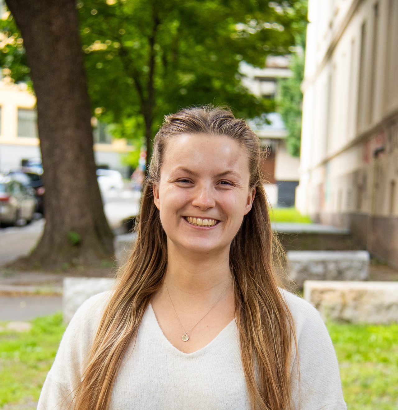 Marie smiler bredt mot kameraet med langt blondt hår som flagrer i vinden. Hun er lys i huden og har på seg en hvit genser og et sølvkjede.