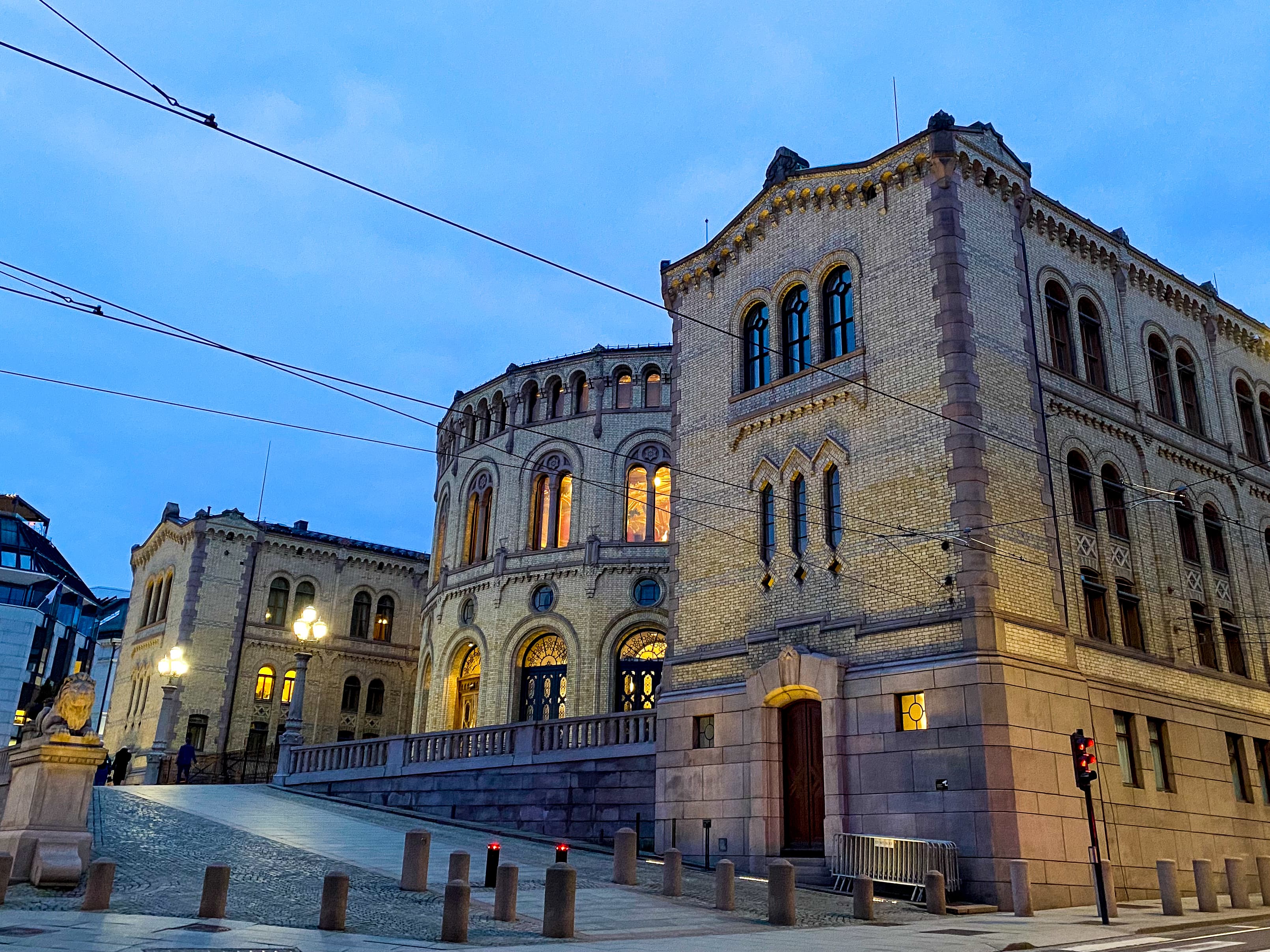 Stortinget fra siden på kveldstid. Det lyser gult i vinduene i kontrast til den mørkeblå klare himmelen. Foto.
